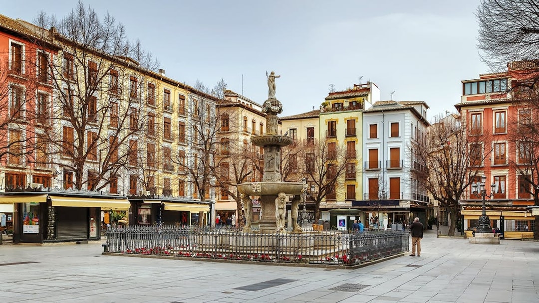 Fountain in Plaza Bib-Rambla, Granada, surrounded by colorful buildings.