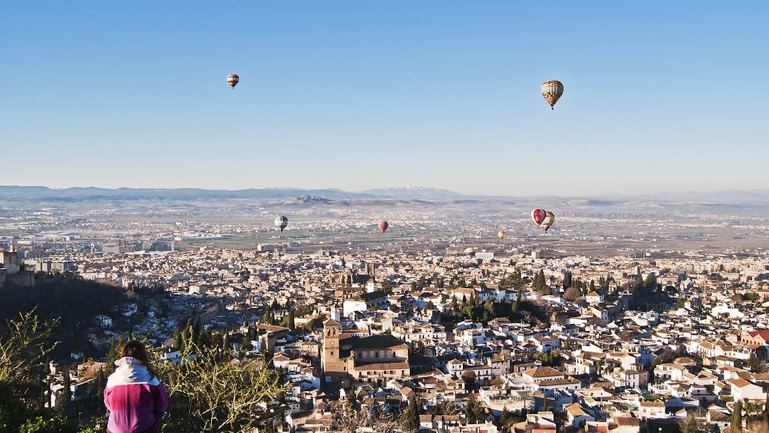 Hot air balloons over Granada with view of Alhambra and cityscape.