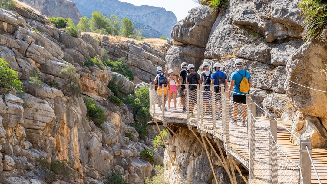 Group walking on Caminito del Rey path in rocky gorge, Andalusia, Spain.