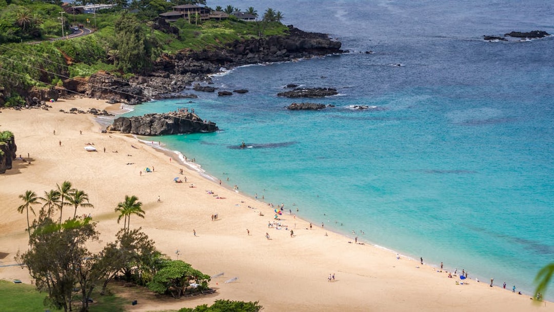 Waimea Bay Beach Park with visitors on sandy shore and turquoise water, Oahu, Hawaii.