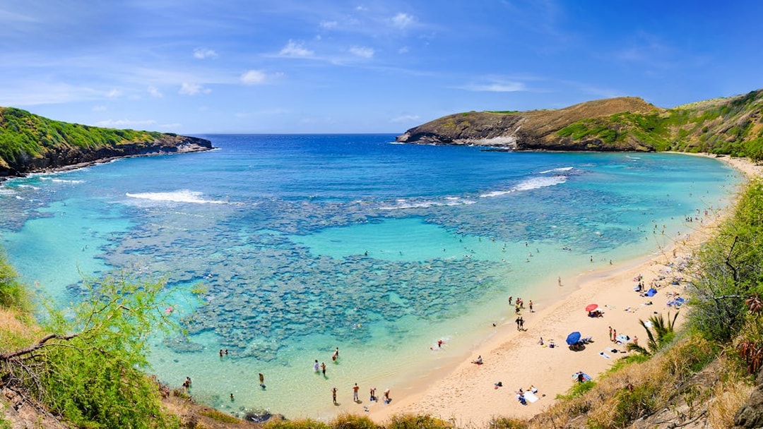 Aerial view of Hanauma Bay, Hawaii, with people on the sandy shore and clear blue water.