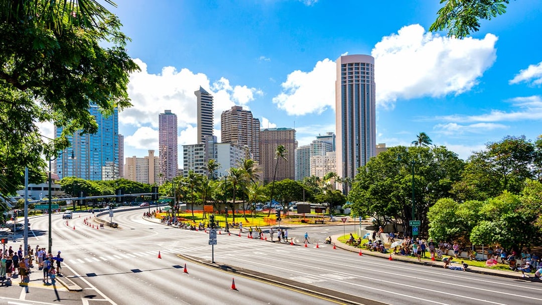Waikiki skyline with high-rise buildings and palm trees, seen from a busy street in Oahu, Hawaii.