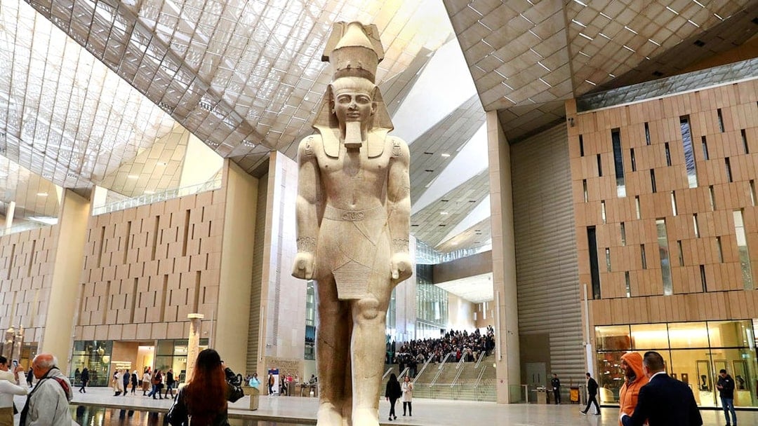 Grand Egyptian Museum interior with large pharaoh statue and visitors exploring.