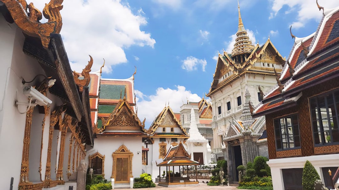 Grand Palace Bangkok courtyard with ornate temple roofs and spires under blue sky.