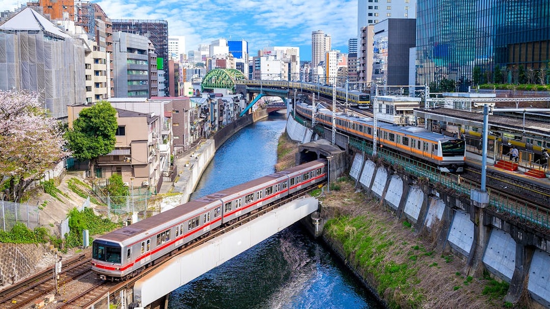 Train crossing a bridge over a river in Tokyo, Japan, with cityscape in the background.