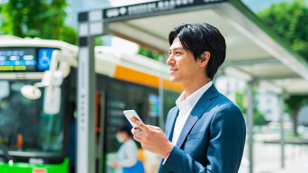 Man using smartphone at Tokyo bus stop with Greater Tokyo Pass.