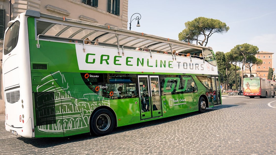 Green Line hop-on hop-off bus in Rome near historic buildings and trees.