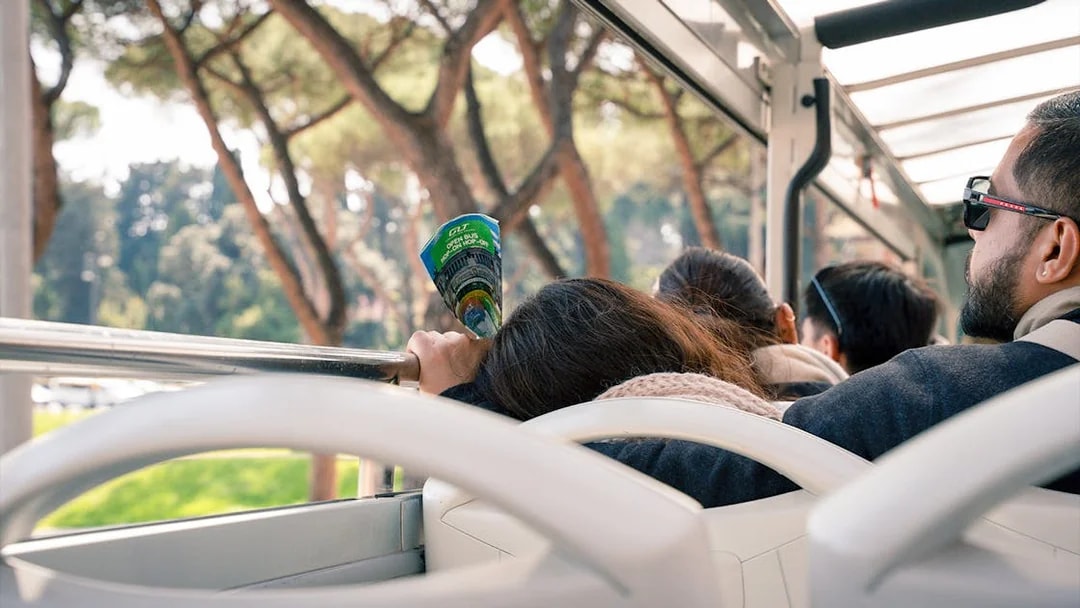 Passengers on Rome hop-on hop-off bus tour holding a brochure, surrounded by trees.