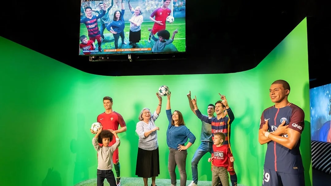 Statues of Lionel Messi and Kylian Mbappe at Grévin Paris wax museum with visitors.
