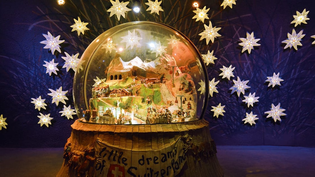 Jungfraujoch snow globe display with Swiss Alps model, surrounded by illuminated edelweiss flowers.