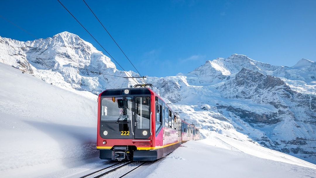 Red train traveling through snowy mountains on route from Grindelwald to Jungfraujoch.