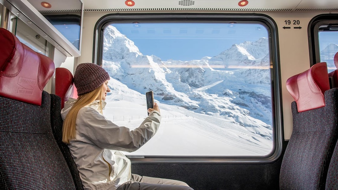 Traveller taking photo from Jungfraubahn train window with snowy Alps view.