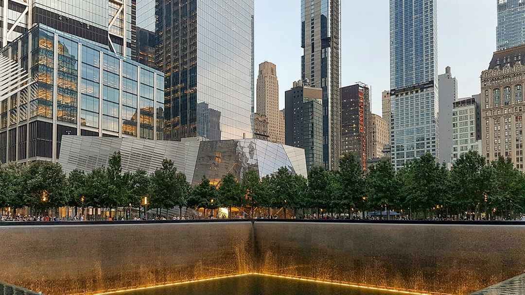 9/11 Memorial reflecting pool with museum entrance and skyscrapers in New York City.
