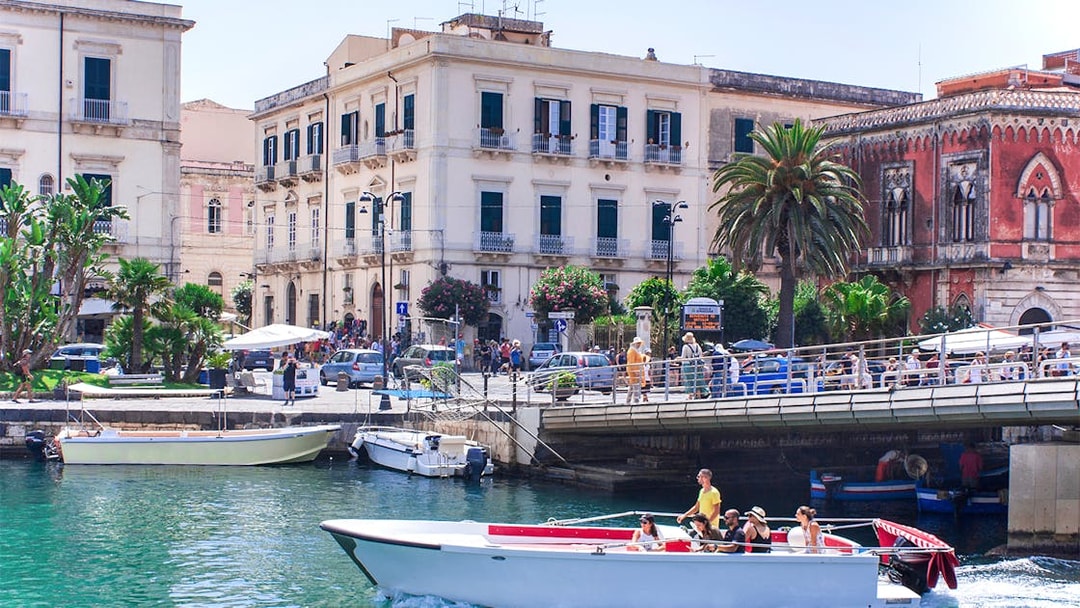 Boat tour passing historic buildings on Ortigia Island, Sicily.