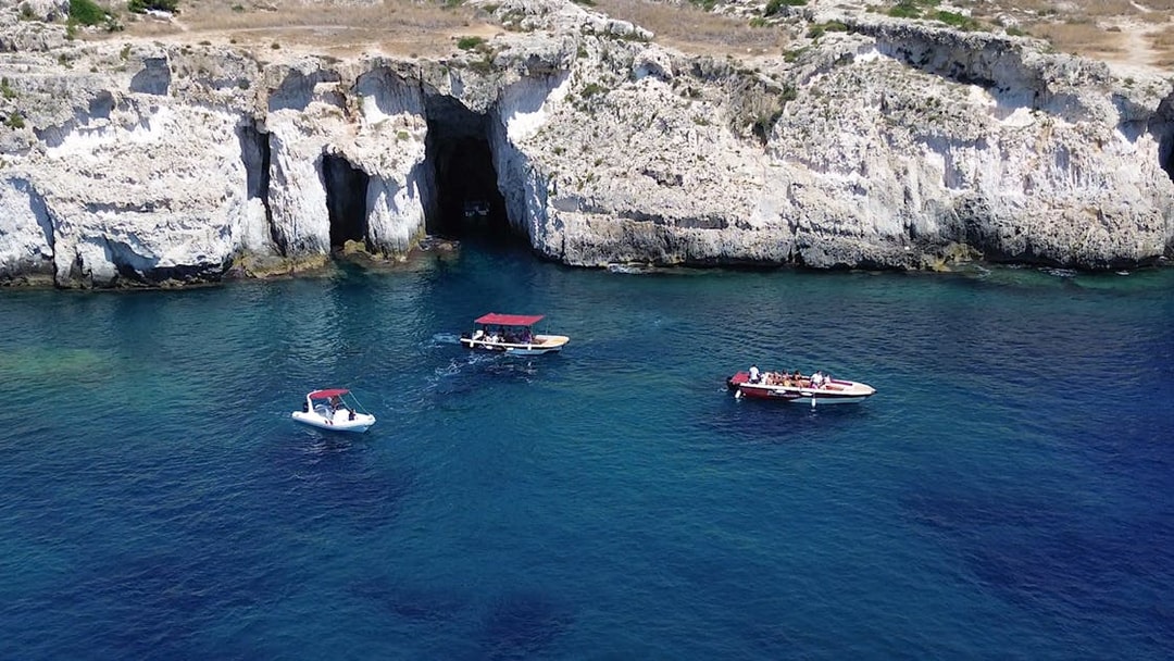 Boats near the grotto at Ortigia Island, Sicily, with rocky cliffs in the background.