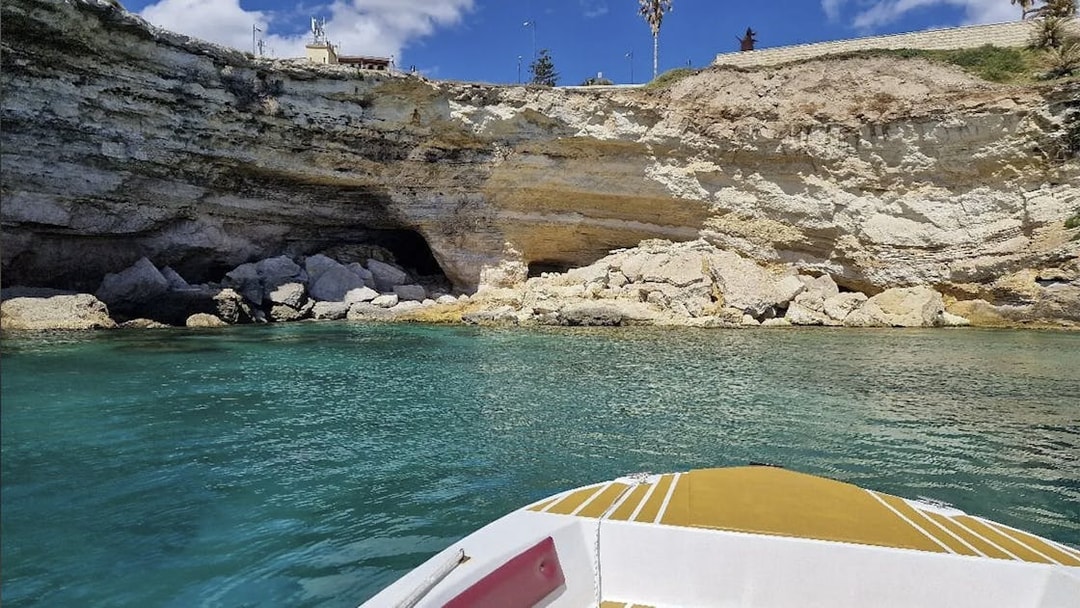 Boat approaching grotto at Ortigia Island, Sicily, with rocky cliffs and clear water.
