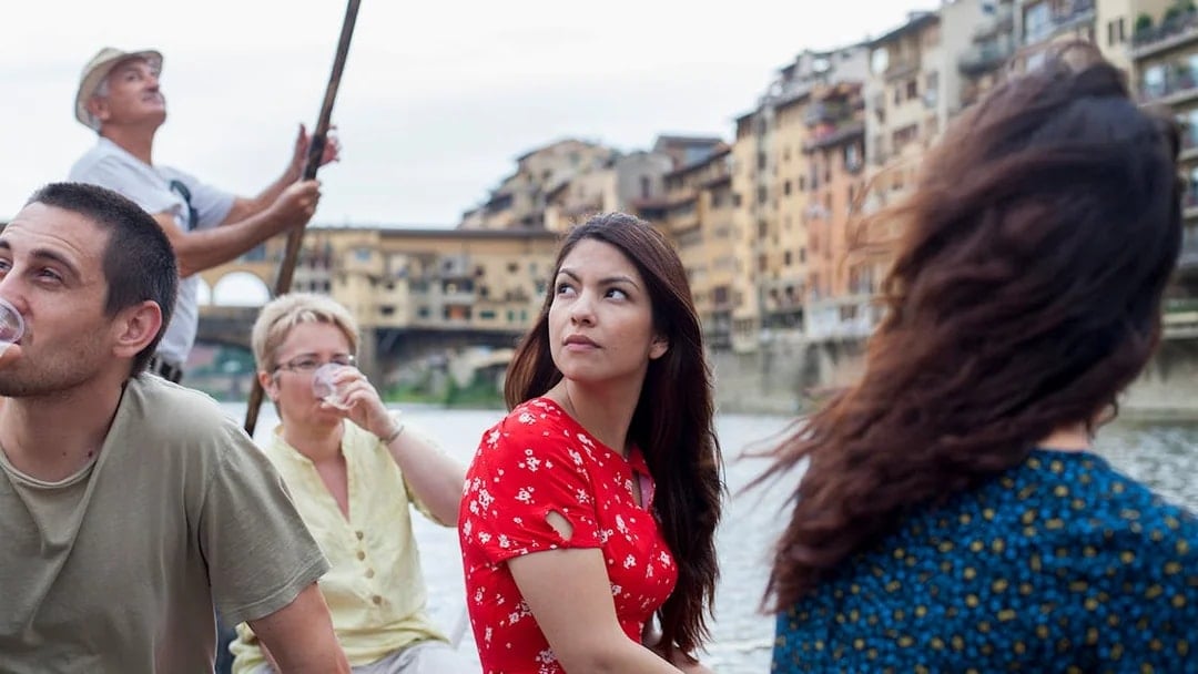 Guided boat tour on a Florentine gondola with tourists on the Arno River.