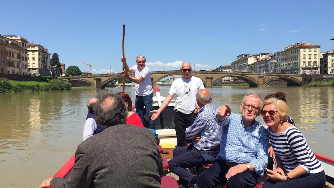 Guided boat tour on a Florentine gondola with tourists enjoying the Arno River view.