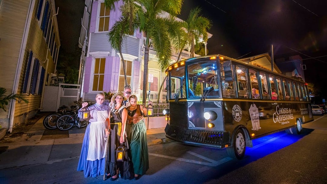 Guided tour group with lanterns beside Ghosts & Gravestones trolley in Savannah at night.