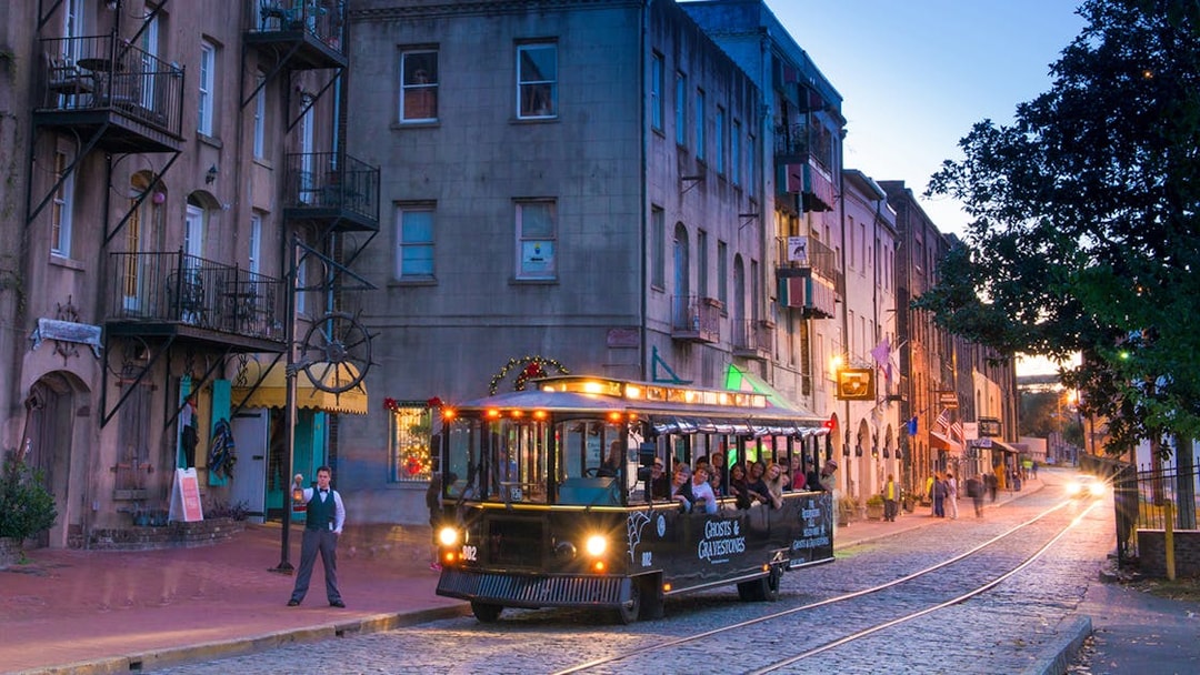 Savannah trolley on cobblestone street during Ghosts & Gravestones tour at dusk.