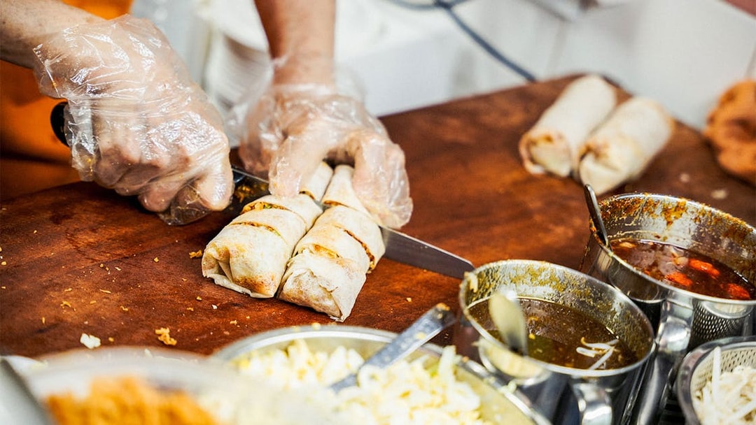 Chef slicing spring rolls on a food tour with sauces and ingredients nearby.