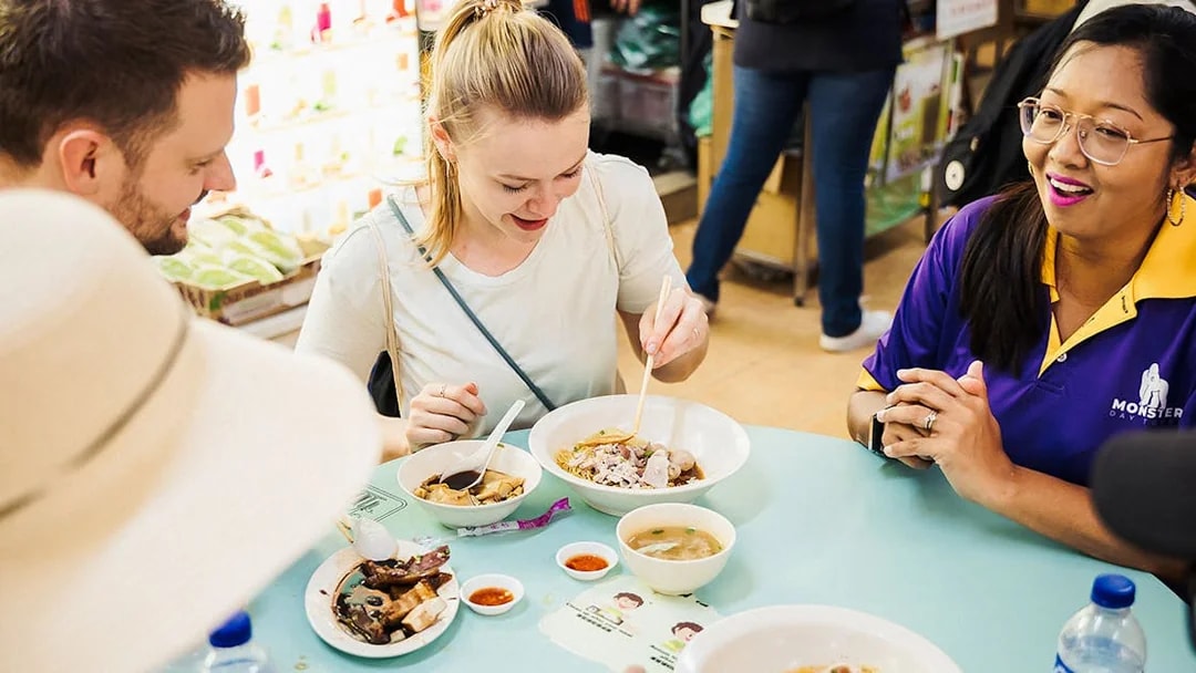 Tourists enjoying local dishes on a guided Michelin and hawker food tour.