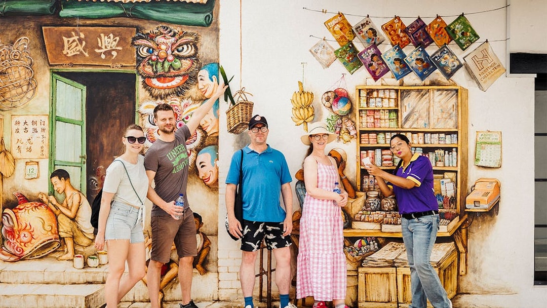 Tourists posing in front of a colorful mural during a guided Michelin and local hawker food tour.