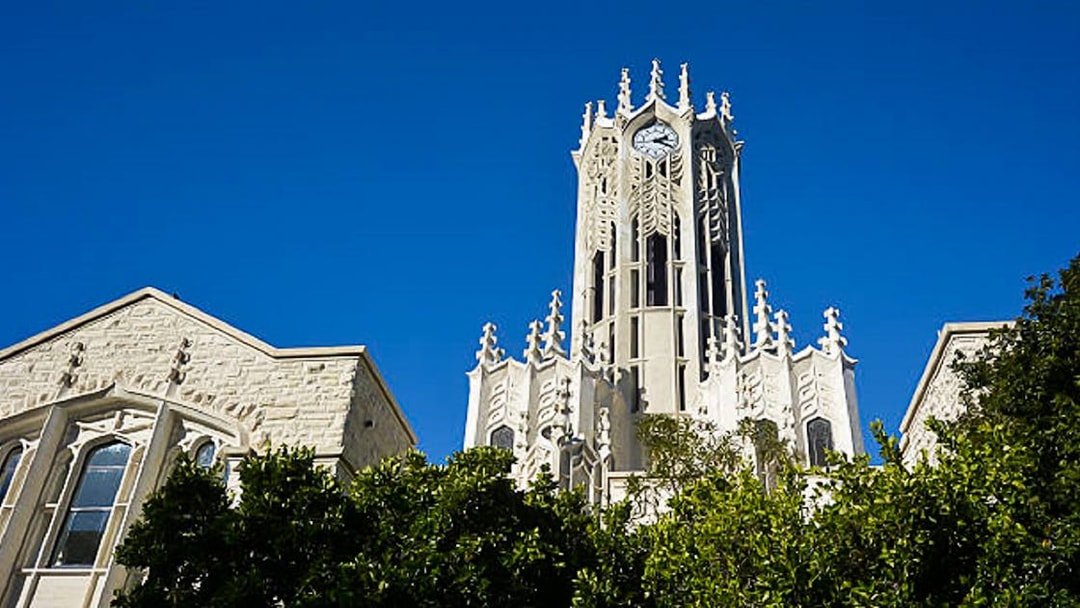 Clock tower of the University of Auckland, New Zealand, against a clear blue sky.