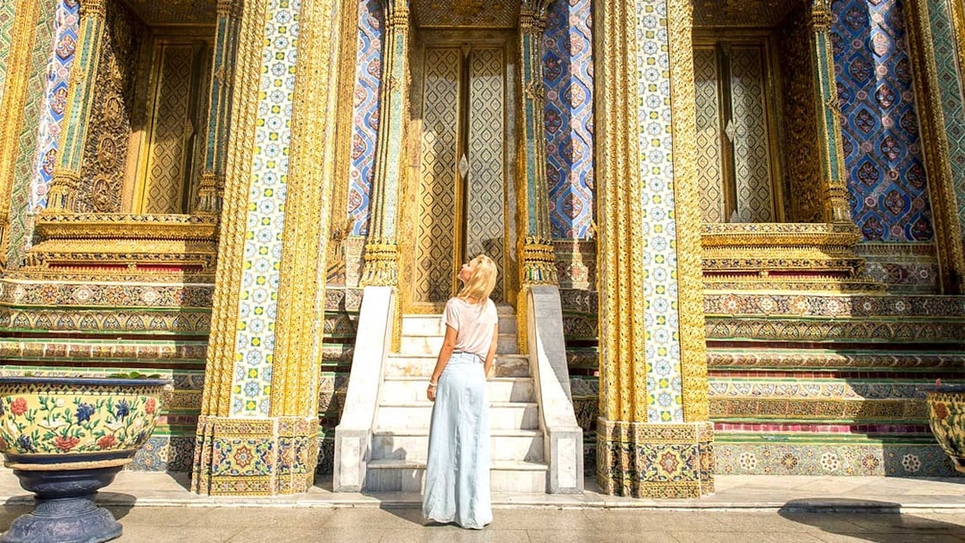 Visitor admiring ornate entrance of Grand Palace temple in Bangkok.