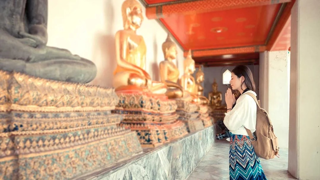 Visitor praying beside Buddha statues at Grand Palace, Bangkok.