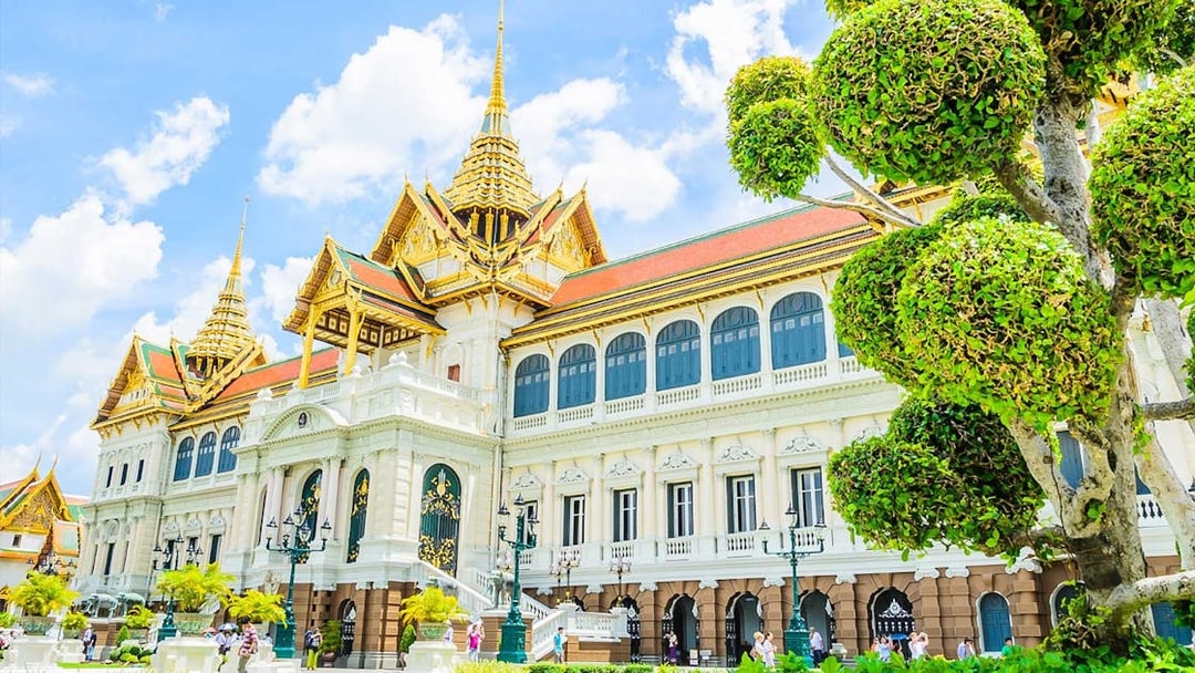 Grand Palace in Bangkok with ornate architecture and manicured trees.