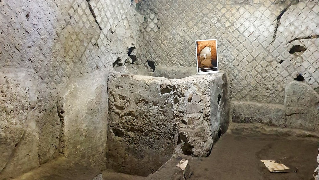 Underground ruins in Naples with ancient stone walls and an informational sign.