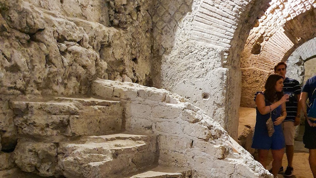 Underground ruins with stone steps and tourists in Naples city tour.