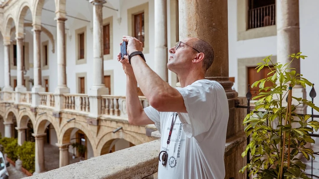Visitor photographing the arches of Palazzo Dei Normanni during a guided tour.