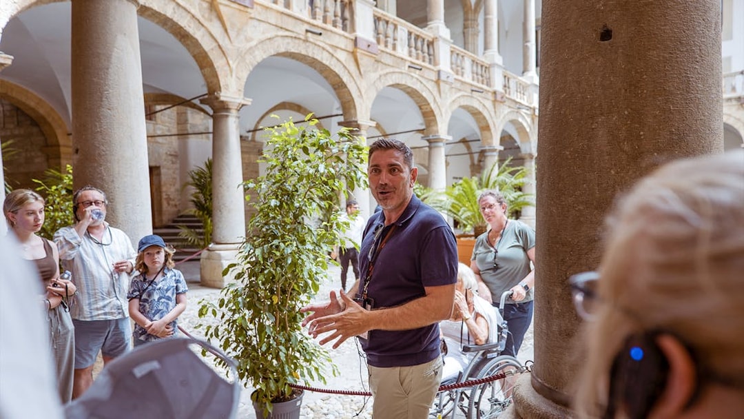 Tour guide explaining history at Palazzo Dei Normanni courtyard, Palermo.