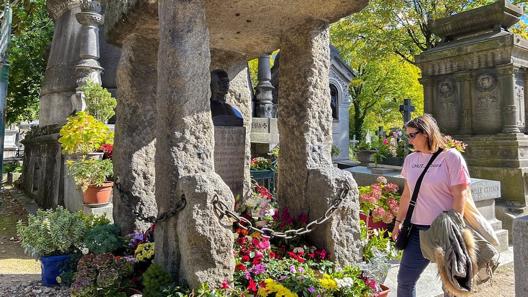Visitor at Père Lachaise cemetery admiring a flower-adorned tombstone.