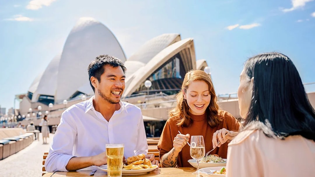 People dining outdoors near Sydney Opera House.