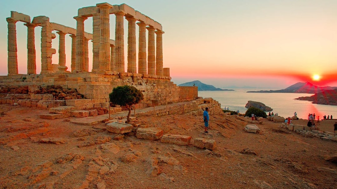 Temple of Poseidon at sunset, Cape Sounion, with tourists exploring the ancient ruins.