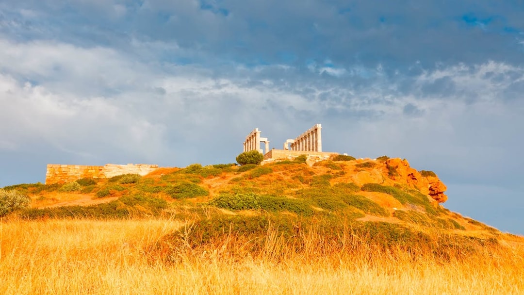 Temple of Poseidon on hilltop at Cape Sounion, Greece, with cloudy sky.