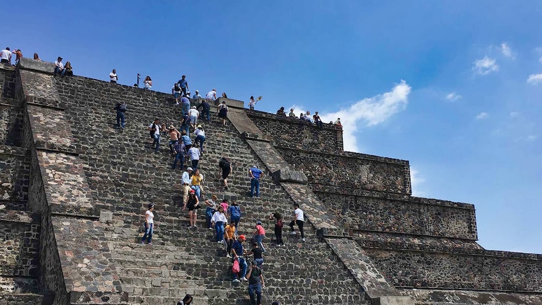 Visitors climbing the Teotihuacán Pyramid steps under a clear sky.