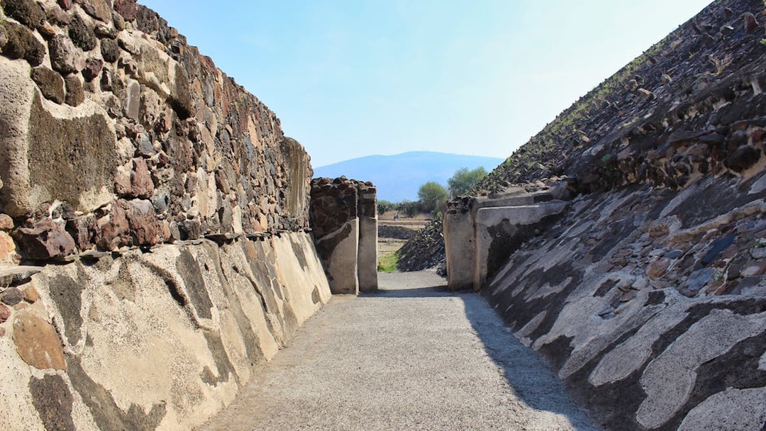 Teotihuacán Pyramid pathway with stone walls and distant mountain view.