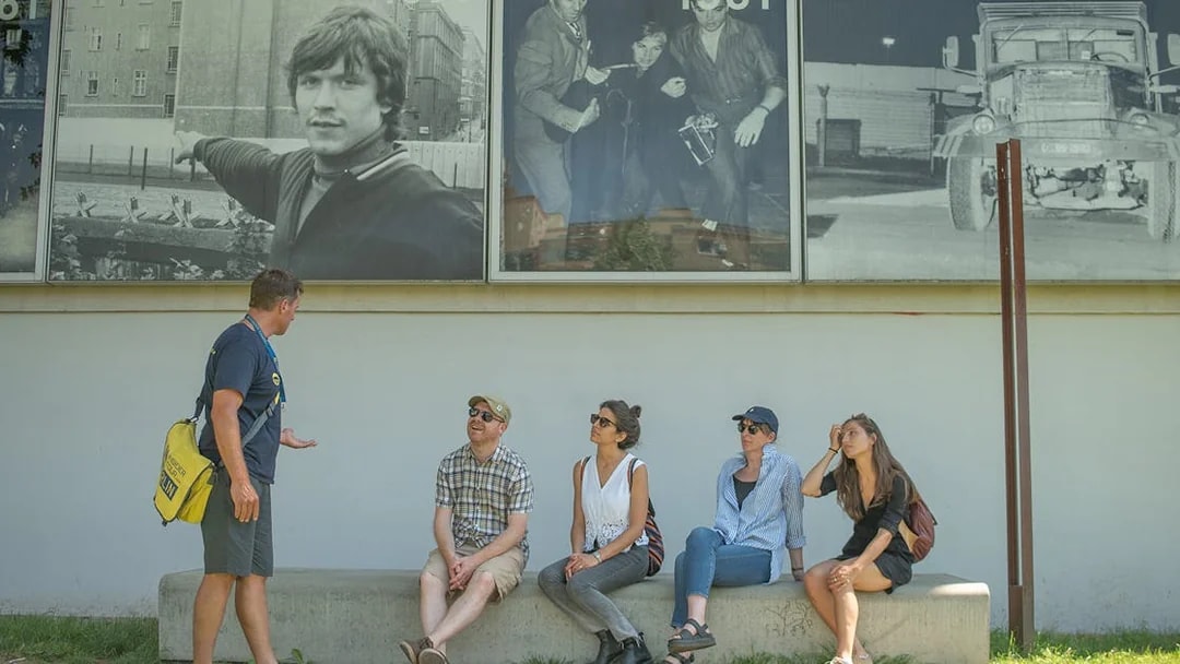 Tour guide explaining Cold War history to a group in front of Berlin Wall photos.