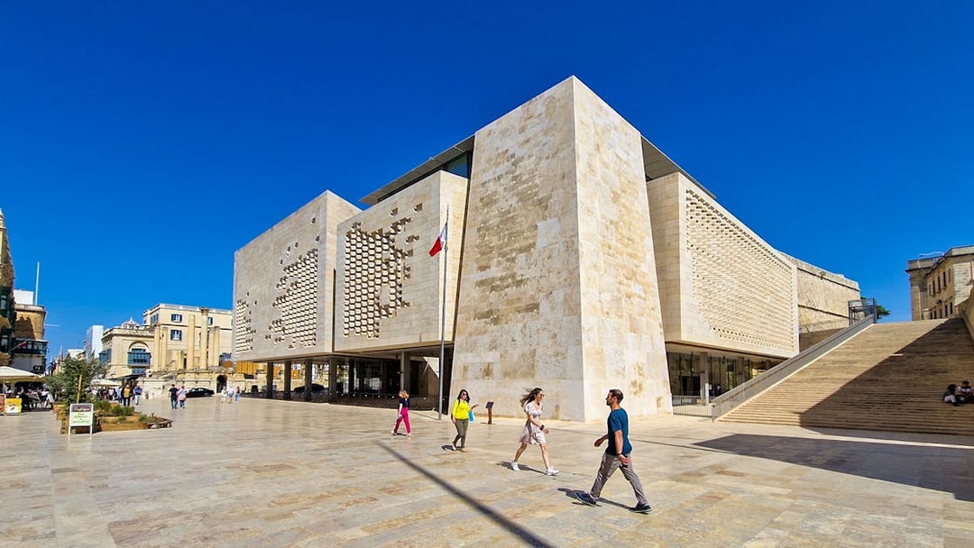 Parliament House in Valletta, Malta, with people walking nearby on a sunny day.