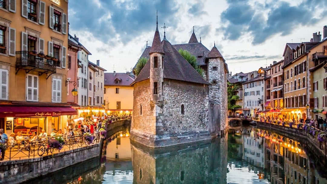 Annecy canal with historic buildings and evening lights reflecting on water.