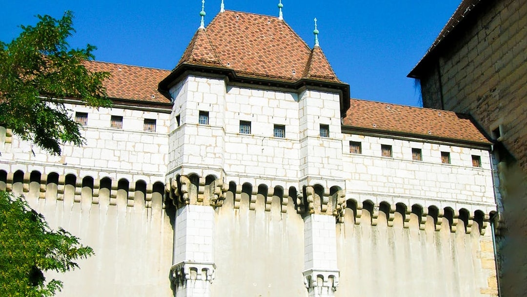 Medieval castle facade in Annecy, France, with stone walls and red-tiled roof.