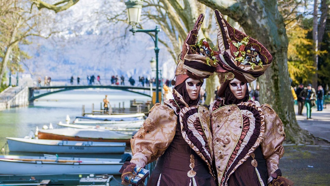 Carnival costumes by Lake Annecy with bridge and boats in the background, Geneva tour.