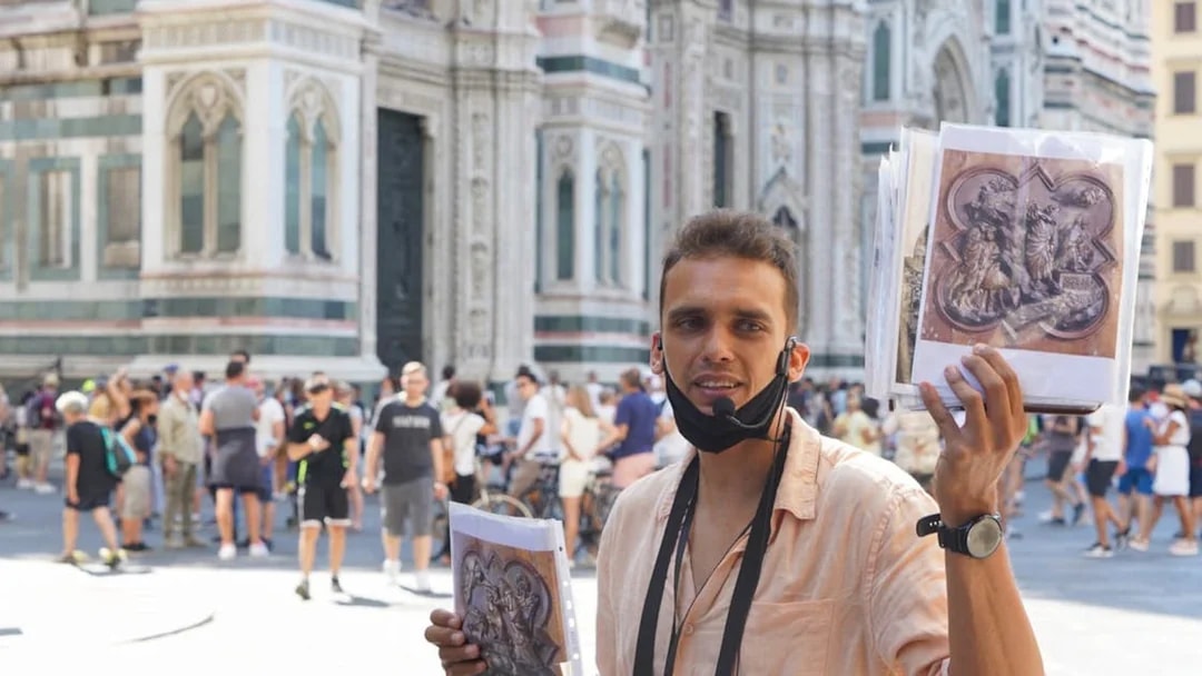 Tour guide in front of Florence Cathedral holding art prints during walking tour.