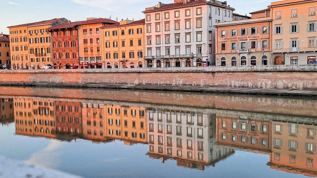 Colorful buildings along the Arno River in Pisa, Italy, reflecting in the water.