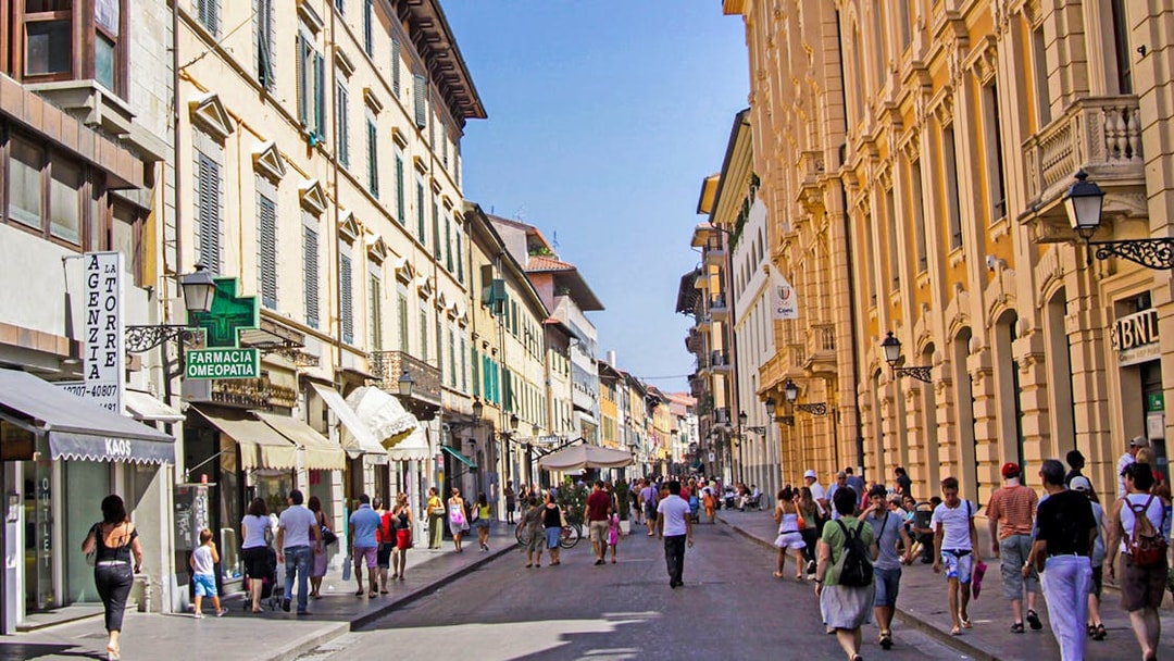 People walking along a bustling street in Pisa, Italy, lined with historic buildings.