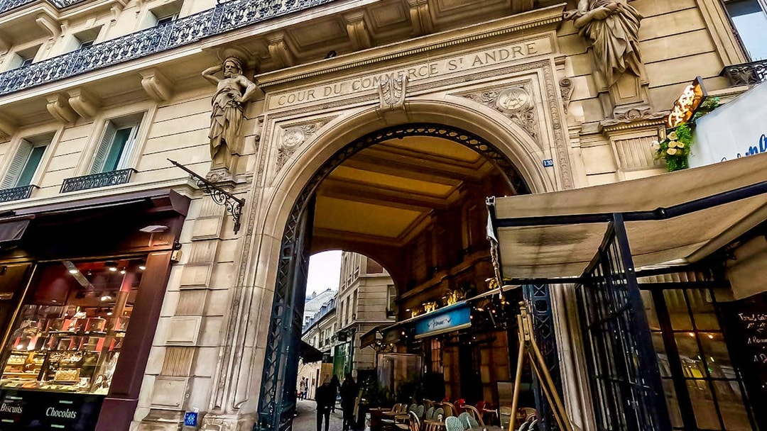 Cour du Commerce Saint-André entrance in Saint-Germain-Des-Prés, Paris, with nearby café tables.